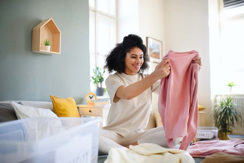 A woman holding a pink sweater while organizing her apartment