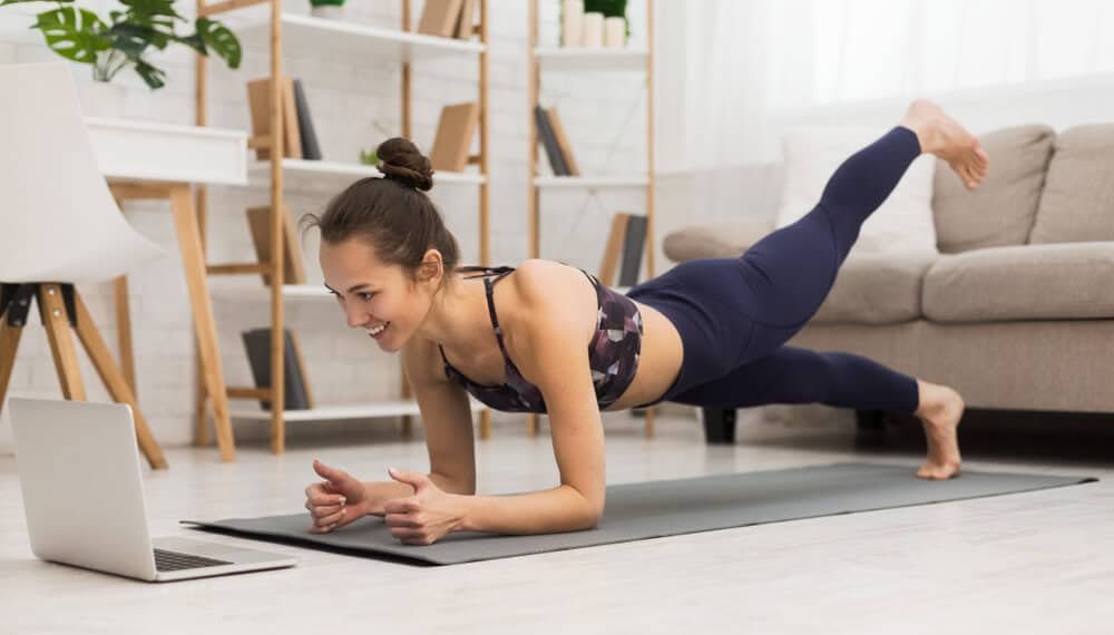 A woman doing home workout while looking in her laptop.