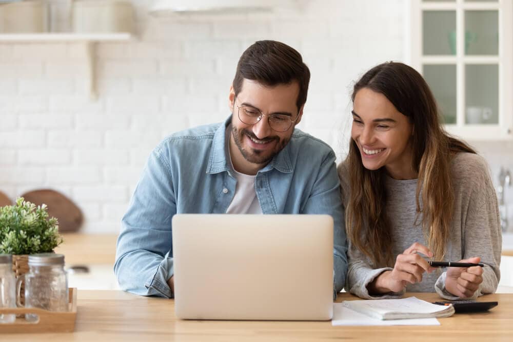 Smiling couple sitting at a table using a laptop together.